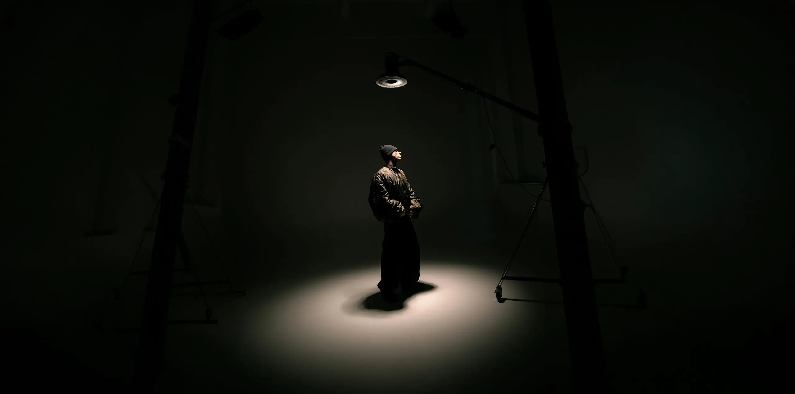 Figura de pie bajo un único foco en un estudio oscuro, campaña VIVA LEGACY